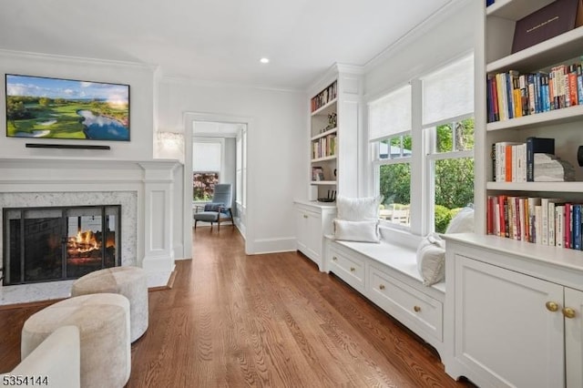 living area featuring recessed lighting, ornamental molding, wood finished floors, and a premium fireplace