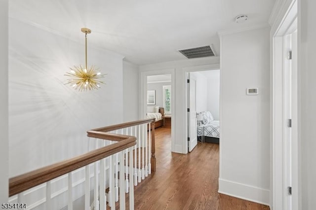 corridor featuring visible vents, wood finished floors, baseboards, a chandelier, and an upstairs landing