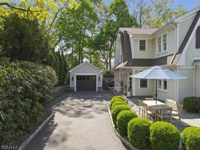 view of front of property with roof with shingles, a gambrel roof, aphalt driveway, a detached garage, and an outdoor structure