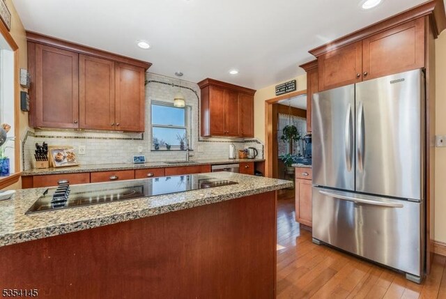 kitchen with backsplash, appliances with stainless steel finishes, light stone countertops, a sink, and light wood finished floors
