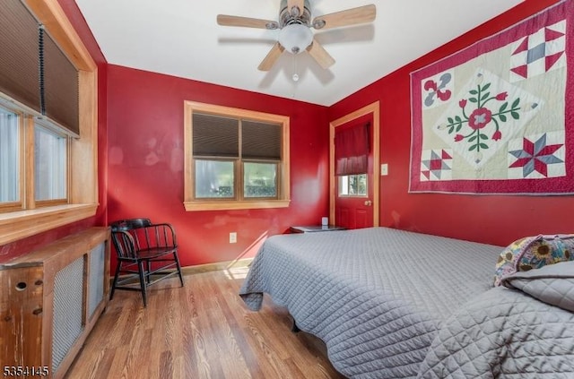 bedroom with a ceiling fan, baseboards, multiple windows, and wood finished floors