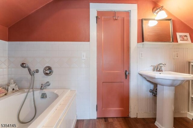 bathroom with a sink, tiled tub, wood finished floors, and lofted ceiling