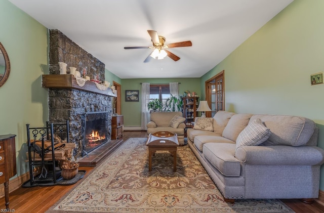 living room featuring a fireplace, a ceiling fan, a baseboard heating unit, and wood finished floors