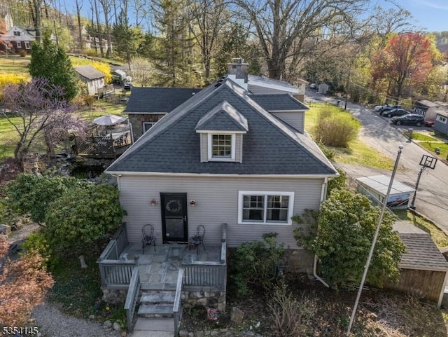 back of property featuring a deck, a chimney, and roof with shingles