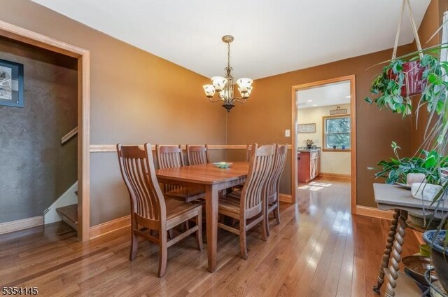 dining room with an inviting chandelier, light wood finished floors, baseboards, and stairway