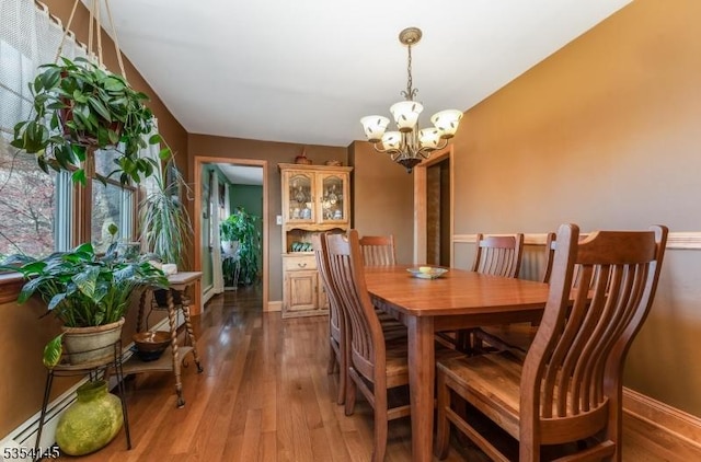 dining area featuring baseboards, a baseboard radiator, wood-type flooring, and a notable chandelier