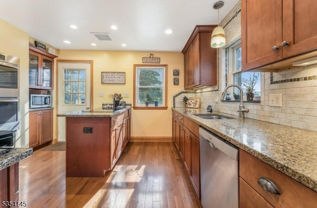 kitchen with brown cabinetry, hardwood / wood-style floors, a sink, dark stone countertops, and appliances with stainless steel finishes