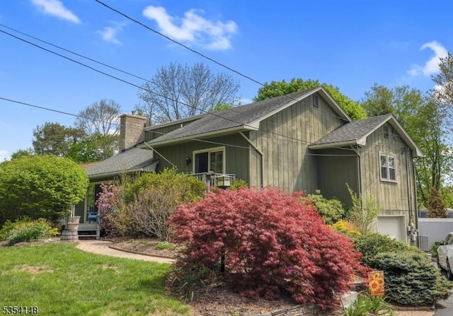 view of side of home with roof with shingles, a chimney, and a yard