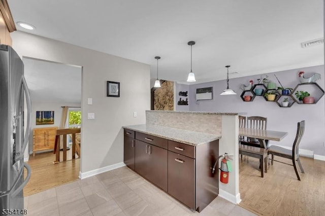 kitchen with a peninsula, dark brown cabinetry, stainless steel fridge, and baseboards