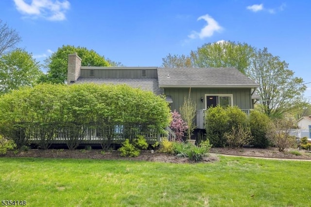 view of front facade featuring board and batten siding, a deck, a chimney, and a front yard
