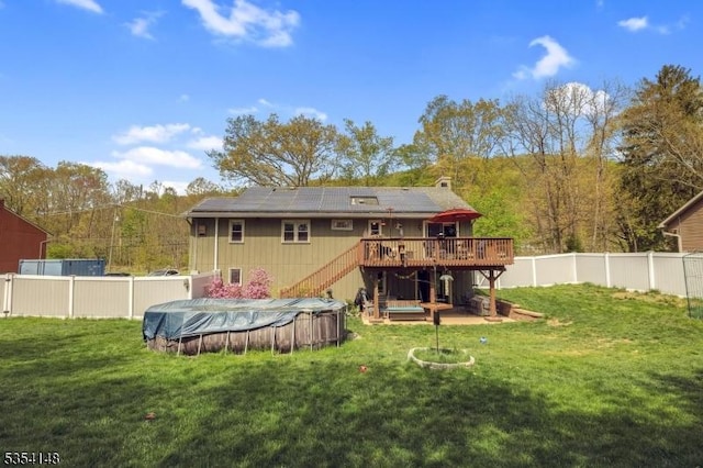 rear view of property featuring a wooden deck, stairway, a fenced backyard, roof mounted solar panels, and a yard