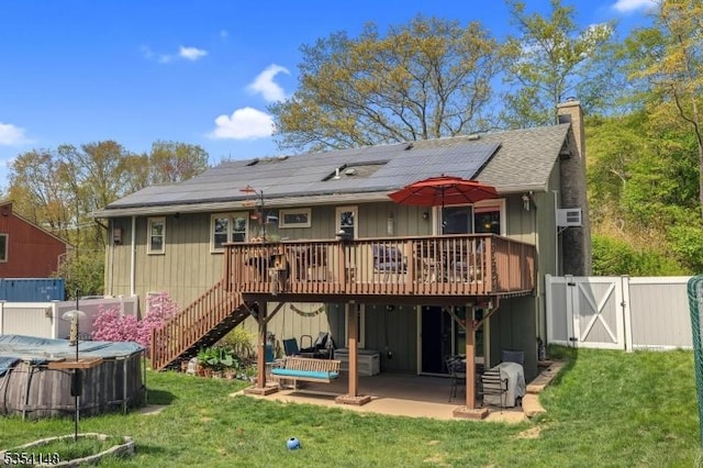 back of house with solar panels, a deck, a gate, a yard, and a patio