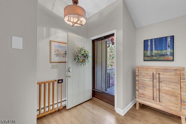 foyer entrance featuring vaulted ceiling, wood finished floors, baseboards, a baseboard heating unit, and a chandelier