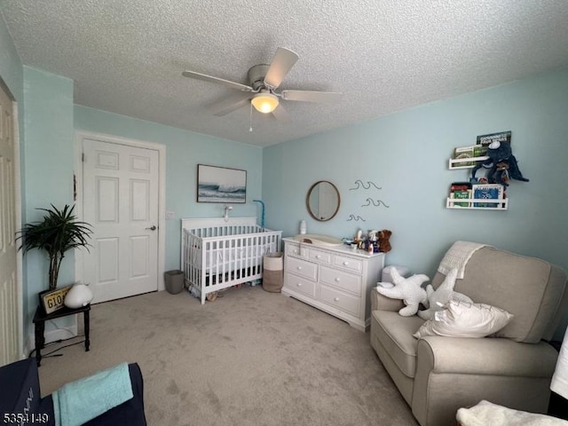 bedroom with a nursery area, ceiling fan, light carpet, and a textured ceiling