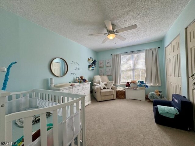 carpeted bedroom featuring a ceiling fan, a textured ceiling, and a nursery area