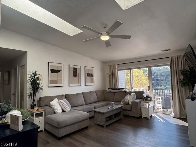 living area with dark wood-style flooring, ceiling fan, visible vents, and vaulted ceiling with skylight