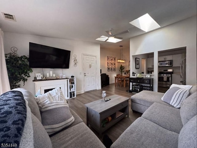 living area featuring ceiling fan, baseboards, wood finished floors, a skylight, and visible vents