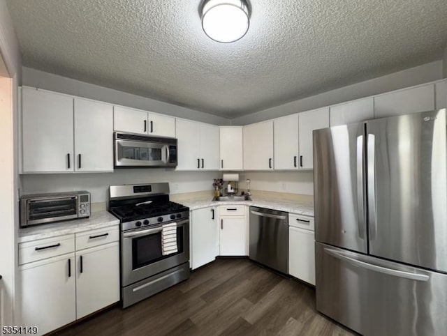 kitchen with a toaster, dark wood-style floors, light countertops, a textured ceiling, and appliances with stainless steel finishes