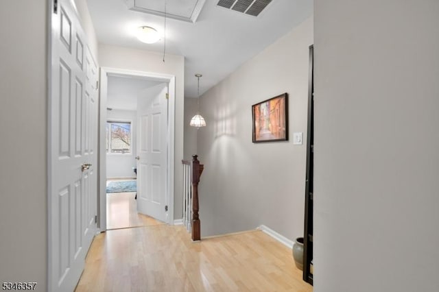 corridor featuring visible vents, attic access, light wood-style floors, and baseboards