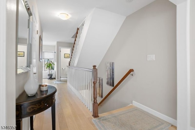 hallway with baseboards, an upstairs landing, and light wood-type flooring
