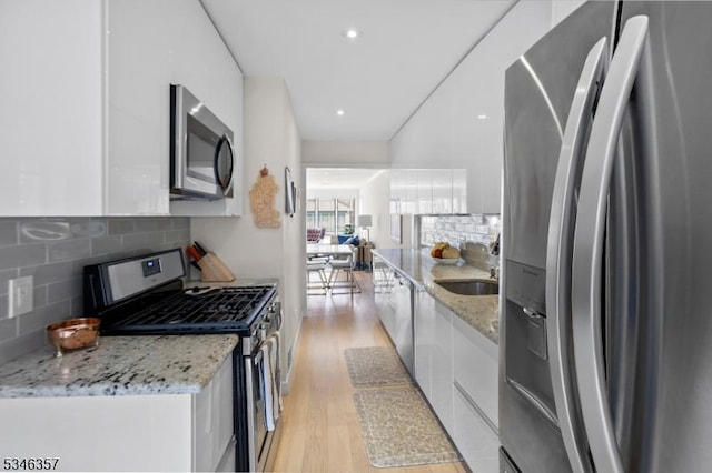 kitchen featuring modern cabinets, light wood-type flooring, white cabinetry, a sink, and stainless steel appliances