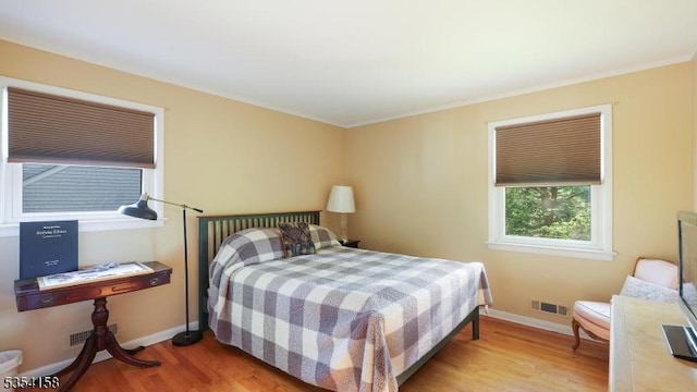bedroom featuring light wood-style floors, baseboards, crown molding, and visible vents