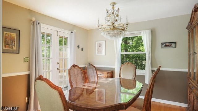 dining space featuring baseboards, a notable chandelier, french doors, and wood finished floors
