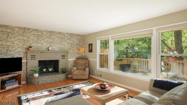 living area with baseboards, plenty of natural light, a fireplace with raised hearth, and wood finished floors