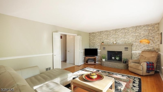 living area featuring a fireplace with raised hearth, light wood finished floors, and visible vents