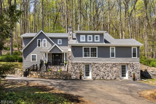 view of front facade with a chimney, aphalt driveway, stone siding, and a porch