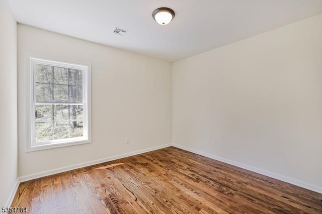 empty room featuring baseboards, visible vents, and wood finished floors