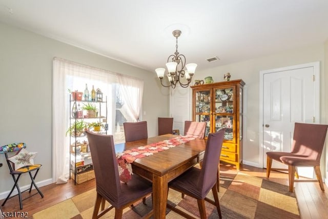 dining room with light wood-style floors, baseboards, visible vents, and a notable chandelier