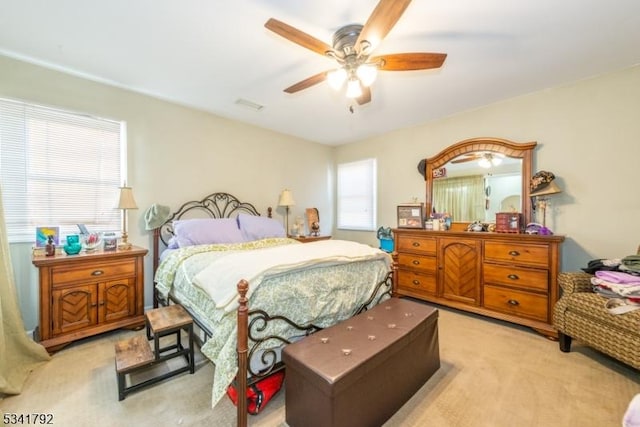 bedroom with light colored carpet, a ceiling fan, and visible vents