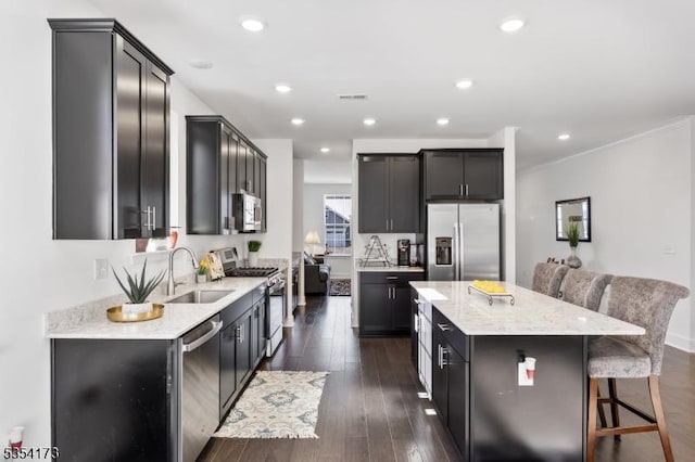 kitchen with a center island, dark wood-type flooring, light stone counters, a sink, and appliances with stainless steel finishes