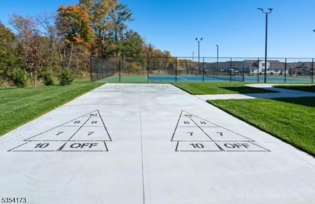 view of home's community featuring fence, a tennis court, a lawn, and shuffleboard