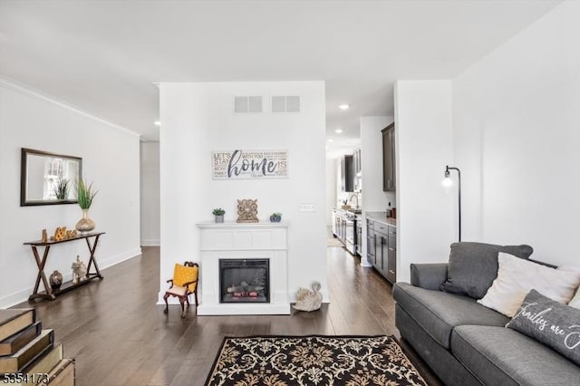 living room featuring dark wood-type flooring, recessed lighting, a glass covered fireplace, and visible vents