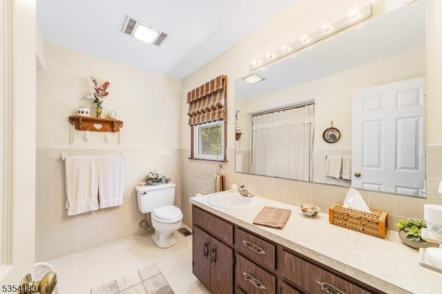 bathroom with visible vents, vanity, wainscoting, toilet, and tile walls