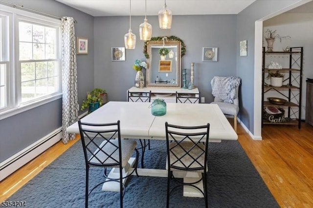 dining space with baseboards, wood finished floors, a healthy amount of sunlight, and baseboard heating