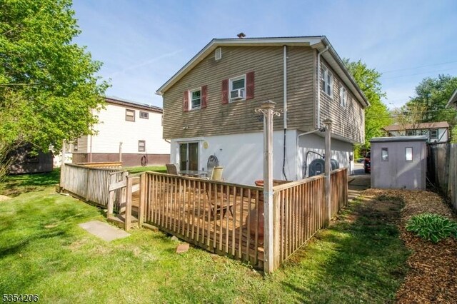 rear view of property with fence, a shed, a deck, an outbuilding, and a lawn