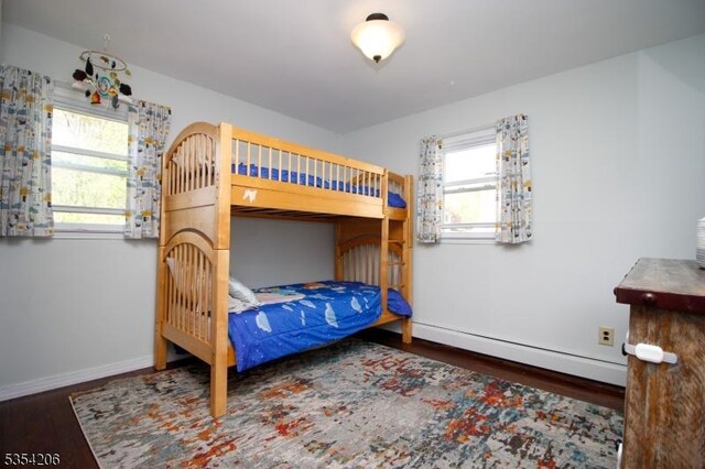 bedroom featuring baseboards, multiple windows, a baseboard heating unit, and wood finished floors