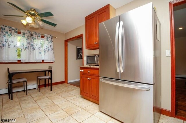 kitchen with light countertops, brown cabinetry, freestanding refrigerator, a ceiling fan, and baseboards