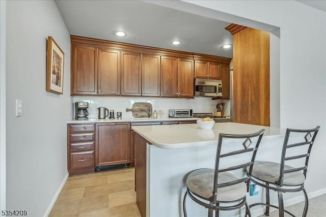 kitchen with light countertops, stainless steel microwave, a breakfast bar, and baseboards