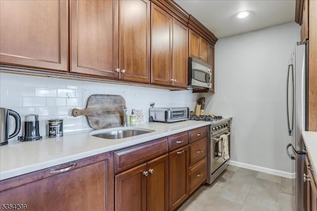 kitchen with brown cabinetry, a toaster, baseboards, light countertops, and appliances with stainless steel finishes