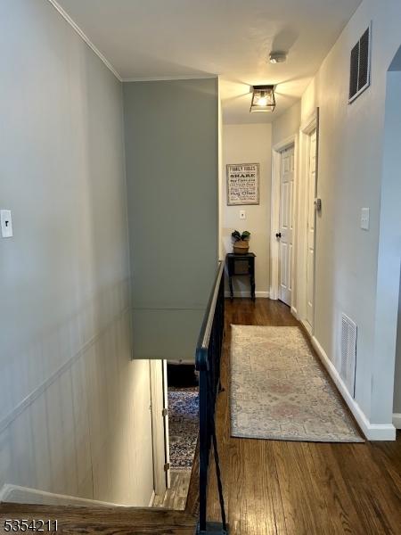 hallway with visible vents, baseboards, and wood finished floors