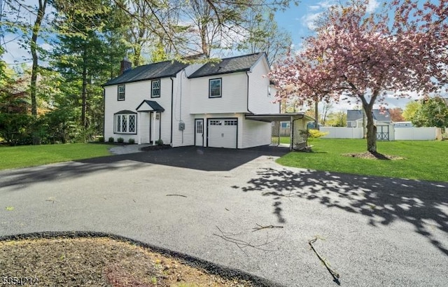 view of front of house with aphalt driveway, a chimney, fence, a front lawn, and an attached garage