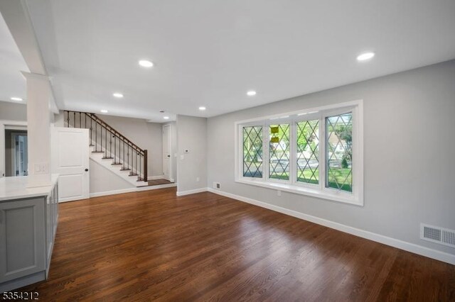 unfurnished living room featuring visible vents, stairs, dark wood-type flooring, and baseboards