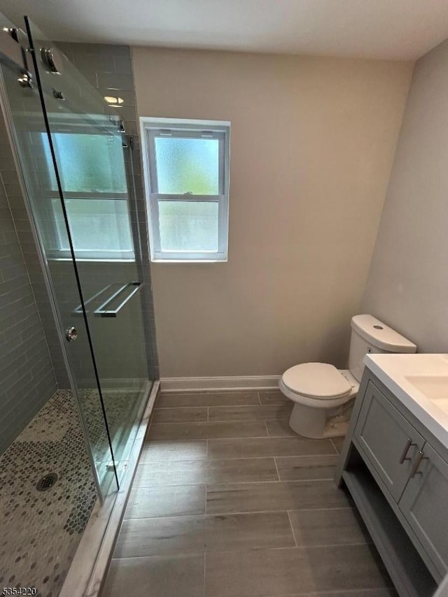 bathroom featuring wood tiled floor, a shower stall, vanity, baseboards, and toilet