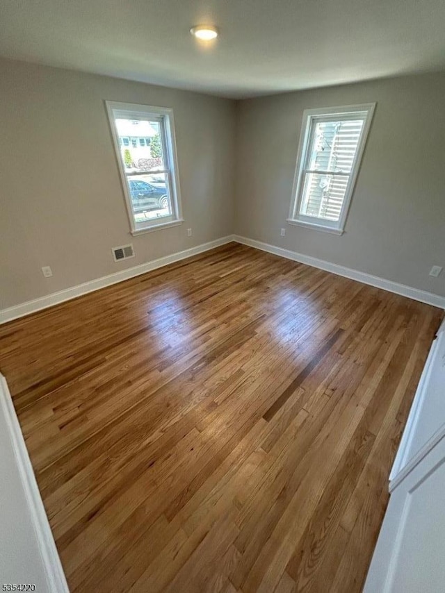 empty room featuring visible vents, plenty of natural light, and wood finished floors