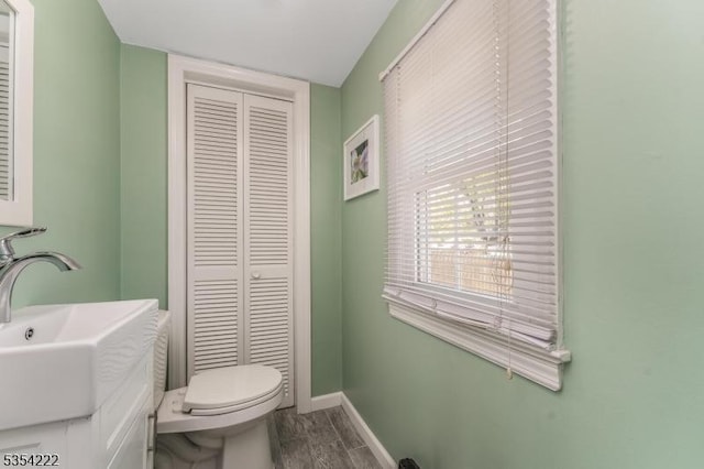 bathroom with baseboards, a closet, toilet, and vanity