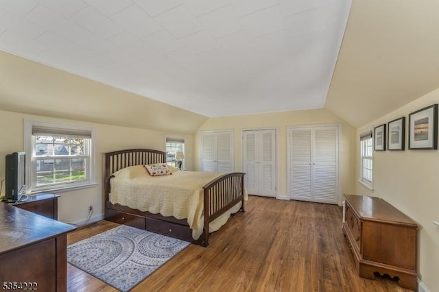 bedroom with two closets, baseboards, vaulted ceiling, and wood finished floors